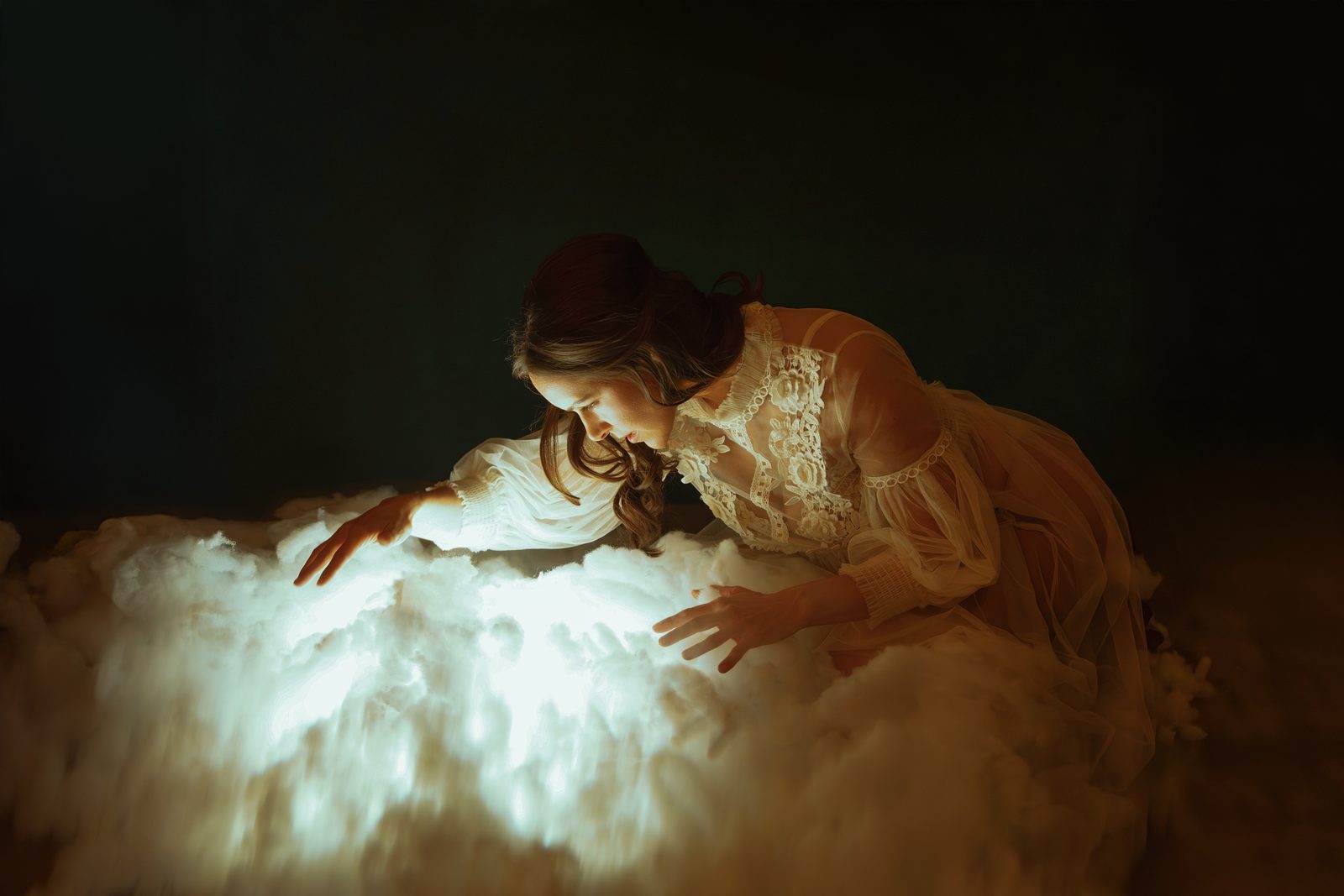JE55IE in a cream lace dress, kneeling over a glowing cloud in a dark room, her hands resting on the light.